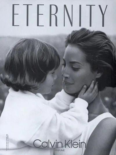 A black-and-white print advertisement for Calvin Klein's Eternity perfume (1992), showing a woman with short dark hair holding a young child who is touching her face; both are wearing white clothing.