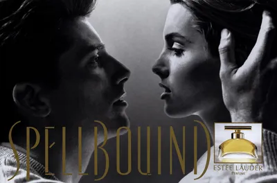 A black-and-white perfume advertisement for Estée Lauder's "Spellbound" fragrance, showing a man and a woman with dark hair facing each other in close proximity, as if about to kiss, with the man's hand raised near the woman's head. The product name "Spellbound" appears in gold text across the lower portion of the image, alongside a small product shot of the perfume bottle, which has a gold cap and a yellow-amber rounded glass body.