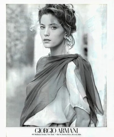 A black-and-white Giorgio Armani print advertisement featuring a woman with brown hair loosely pinned up, wearing a white blouse and a sheer, draped scarf or wrap over her shoulders. The ad includes the Giorgio Armani logo and store addresses for New York and Beverly Hills at the bottom.