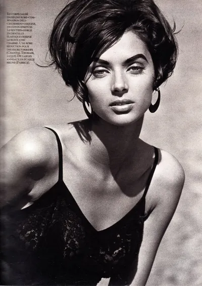 A black-and-white magazine editorial photo of a woman with short dark hair wearing a black lace slip dress and large hoop earrings, photographed from the chest up. French fashion text appears in the upper left corner, referencing Chantal Thomass and Fabrice accessories.