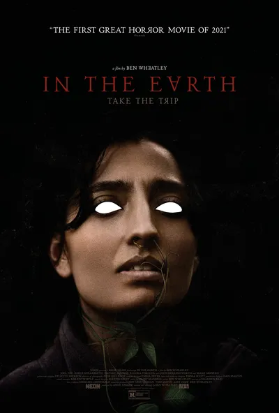 This is a movie poster for the horror film In the Earth, directed by Ben Wheatley. It shows a close-up portrait of a woman with dark hair, brown skin, and a nose ring, with her eyes digitally altered to appear as solid white voids, and a green plant stem extending from her mouth or neck area against a dark background.