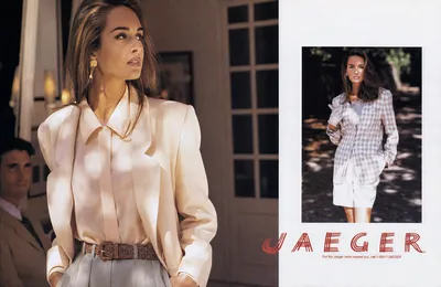 A vintage Jaeger fashion advertisement (magazine spread) featuring a woman with long brown hair in two separate photos. In the larger left photo, she wears a cream/ivory satin blouse with structured shoulders and a woven brown leather belt, with a man in a tan jacket partially visible in the background. In the smaller right photo, the same woman wears a pink-and-white plaid or check jacket over a white top with white shorts and white gloves, standing outdoors in dappled light. The Jaeger brand logo appears in red lettering at the bottom right, with a phone number reading "1-800-7-JAEGER."