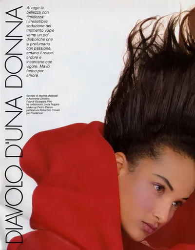 This is a vintage Italian fashion magazine spread titled Diavolo d'una Donna, featuring a close-up portrait of a young woman with dark brown hair styled dramatically upswept. She is wearing or wrapped in a bold red garment, and her face is turned slightly toward the camera with a calm expression. The page includes Italian text and photo credits on the left side.