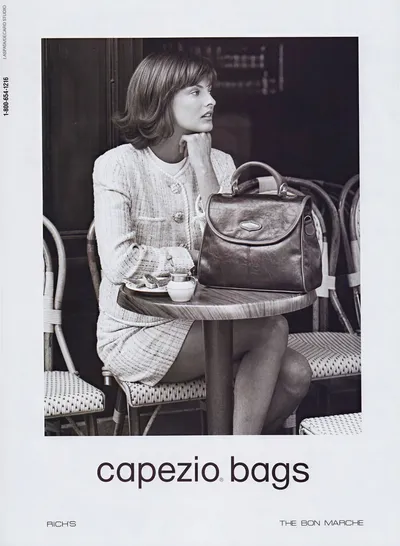 This is a black and white print advertisement for Capezio Bags, retailed at Rich's and The Bon Marche. A woman with chin-length brown hair sits at a small round cafe table, resting her chin on one hand and looking to the side. She wears a textured tweed-style jacket and matching skirt in a light color. A structured leather handbag with a top handle sits on the table beside a small coffee cup and saucer. The setting appears to be an outdoor or bistro-style cafe with wicker chairs.