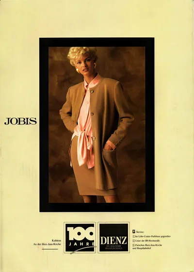 This is a vintage fashion advertisement for the brand Jobis, sold at Dienz clothing store in Koblenz, Germany. A woman with short blonde hair poses against a brown studio backdrop, wearing a tan collarless button-front coat over a pink blouse with a large bow tied at the waist, paired with a tan skirt that falls below the knee.