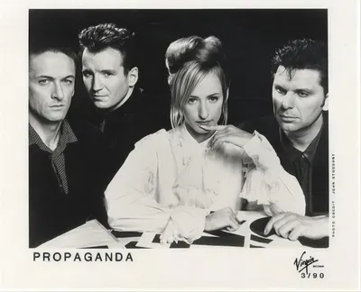 A black-and-white promotional press photo dated 3/90, showing four people — three men and one woman with blonde hair styled in an updo, wearing a white ruffled blouse — posed closely together looking at the camera. The band name "Propaganda" is printed in the lower left, and the Virgin Records logo appears in the lower right.