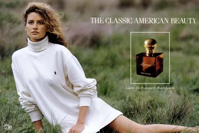 A vintage print advertisement for Lauren fragrance by Ralph Lauren, featuring a woman with curly brown hair wearing an oversized white Polo Ralph Lauren turtleneck sweater, seated in a grassy outdoor setting. The ad includes text reading "The Classic American Beauty" and an image of the perfume bottle — a dark amber square bottle with a gold cap — alongside the caption "Lauren. The Fragrance by Ralph Lauren."