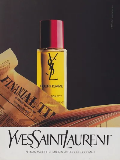 A vintage print advertisement for Yves Saint Laurent "Pour Homme" Eau de Toilette, showing a clear glass bottle with a red and black cap containing golden-yellow liquid, positioned on top of open books and beside a Financial Times newspaper dated January 1987. The YSL logo and product name are printed on the bottle. The brand name "Yves Saint Laurent" appears in large script lettering at the bottom, along with retailer names Neiman Marcus, I. Magnin, and Bergdorf Goodman.