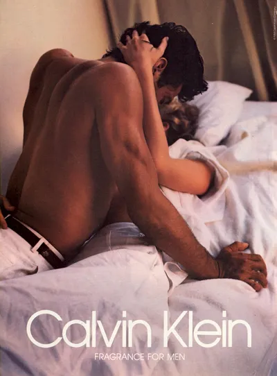 A vintage Calvin Klein Fragrance for Men print advertisement showing a shirtless man with dark hair leaning over a person lying on white bedding, in an intimate pose. The Calvin Klein logo and product description appear at the bottom.