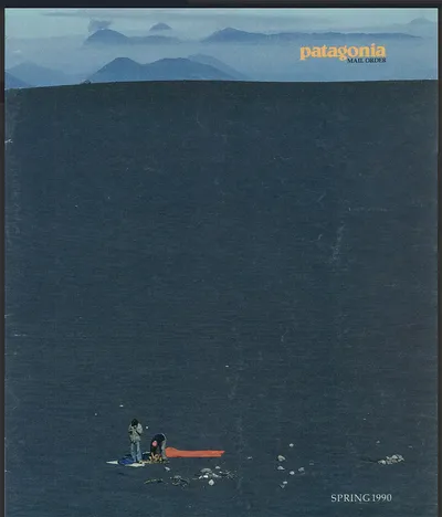 This is a Patagonia Mail Order catalog cover from Spring 1990, showing two small figures camping on a vast dark volcanic slope, with layered blue mountain ridges and what appear to be active volcanoes in the misty background; an orange sleeping bag or tarp is spread on the ground beside them.