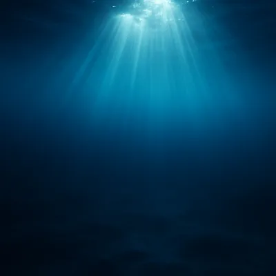 An underwater photograph showing rays of sunlight penetrating the ocean surface from above, casting beams of light into deep blue water that darkens toward the bottom.