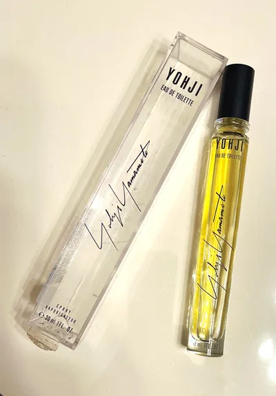 A product photo showing a slim 30ml bottle of Yohji Yamamoto Eau de Toilette with yellow-tinted liquid and a black cap, next to its clear rectangular box, both displaying the Yohji Yamamoto signature in cursive.